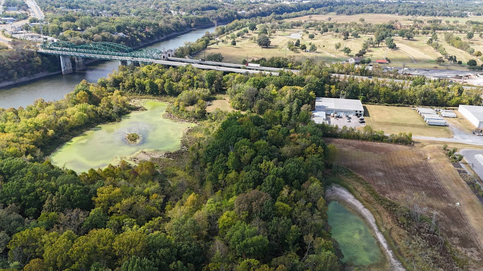 Aerial view of a river, green truss bridge and fields